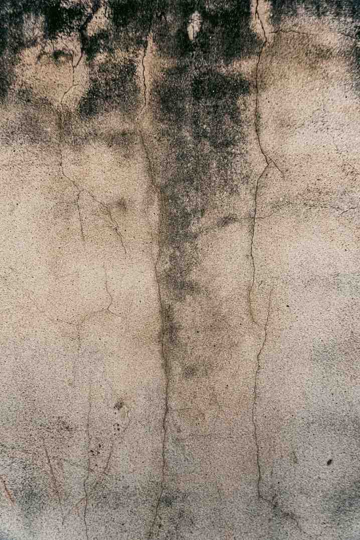 Weathered, beige concrete wall texture with vertical cracks and dark, soot-like stains.