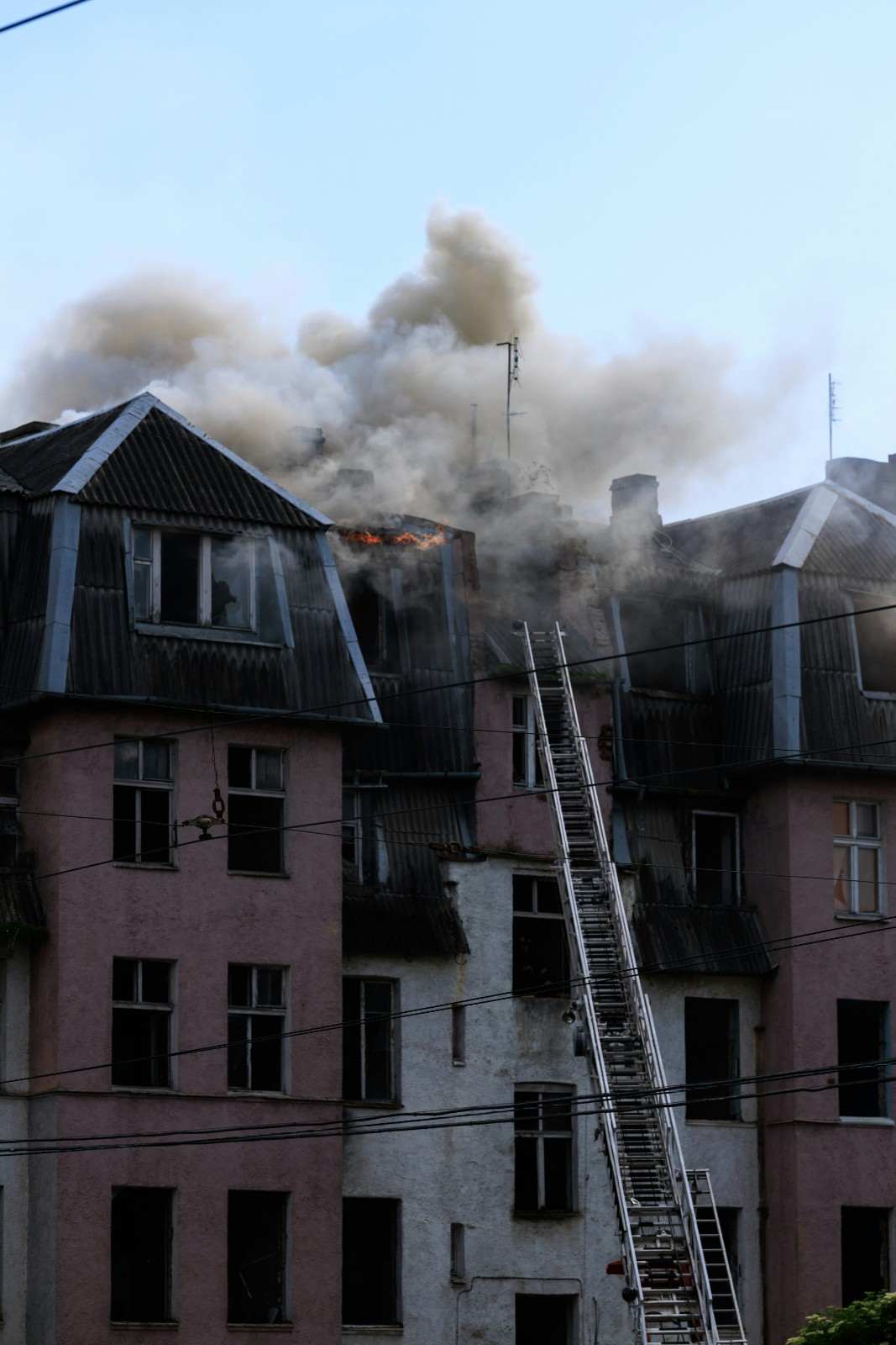 Active fire and thick smoke on an apartment building roof with a fire rescue ladder extended.