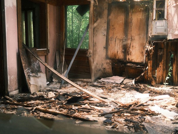 Severely burnt interior room filled with heavy wood debris and destroyed walls from a fire.