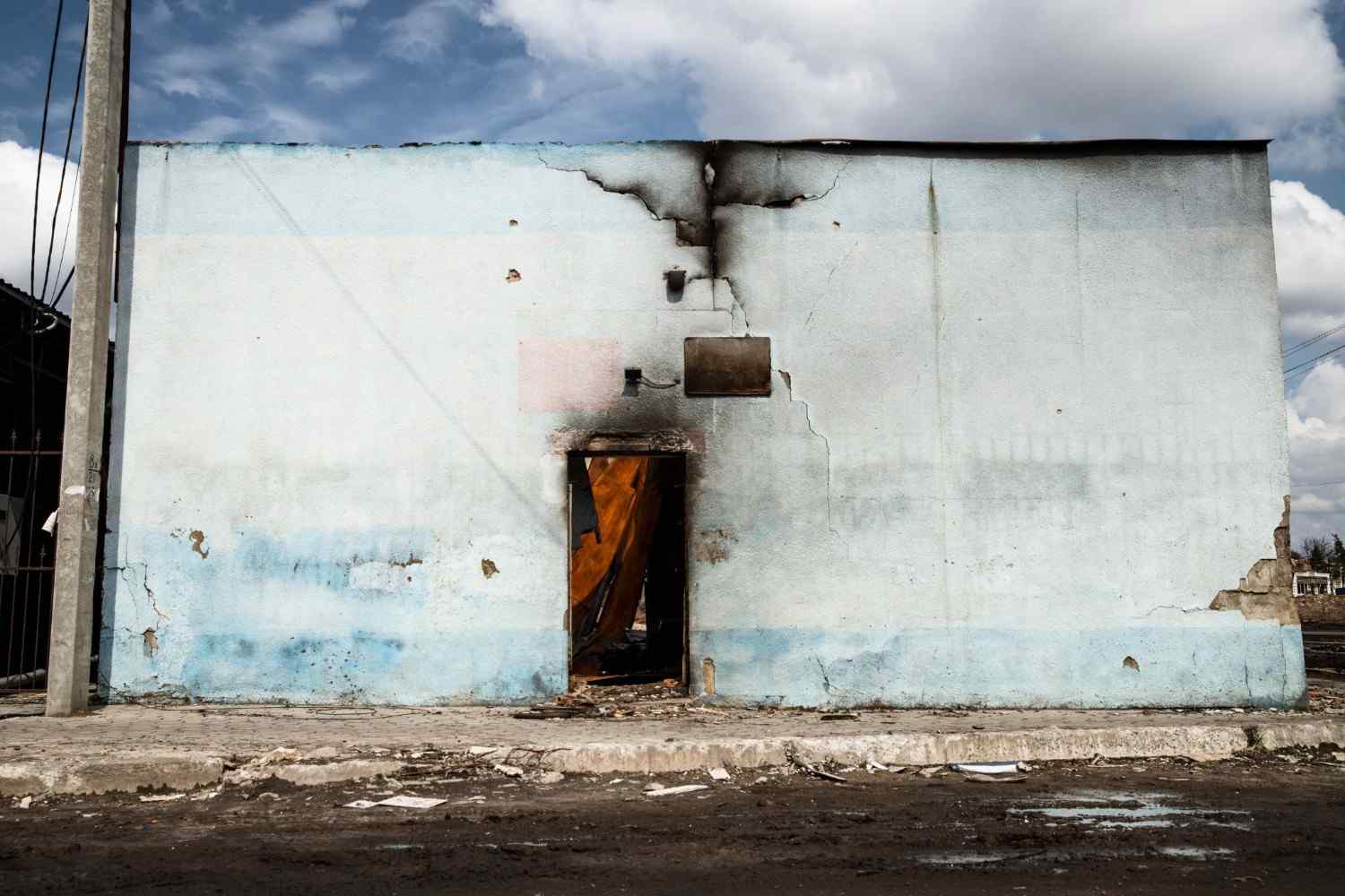 Light blue building exterior showing a burnt doorway, heavy smoke stains, and cracked walls