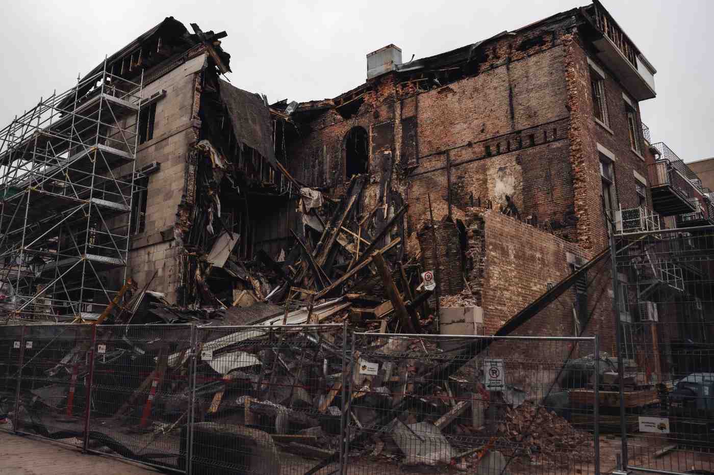 Collapsed brick commercial building showing severe structural fire damage and charred wood debris.