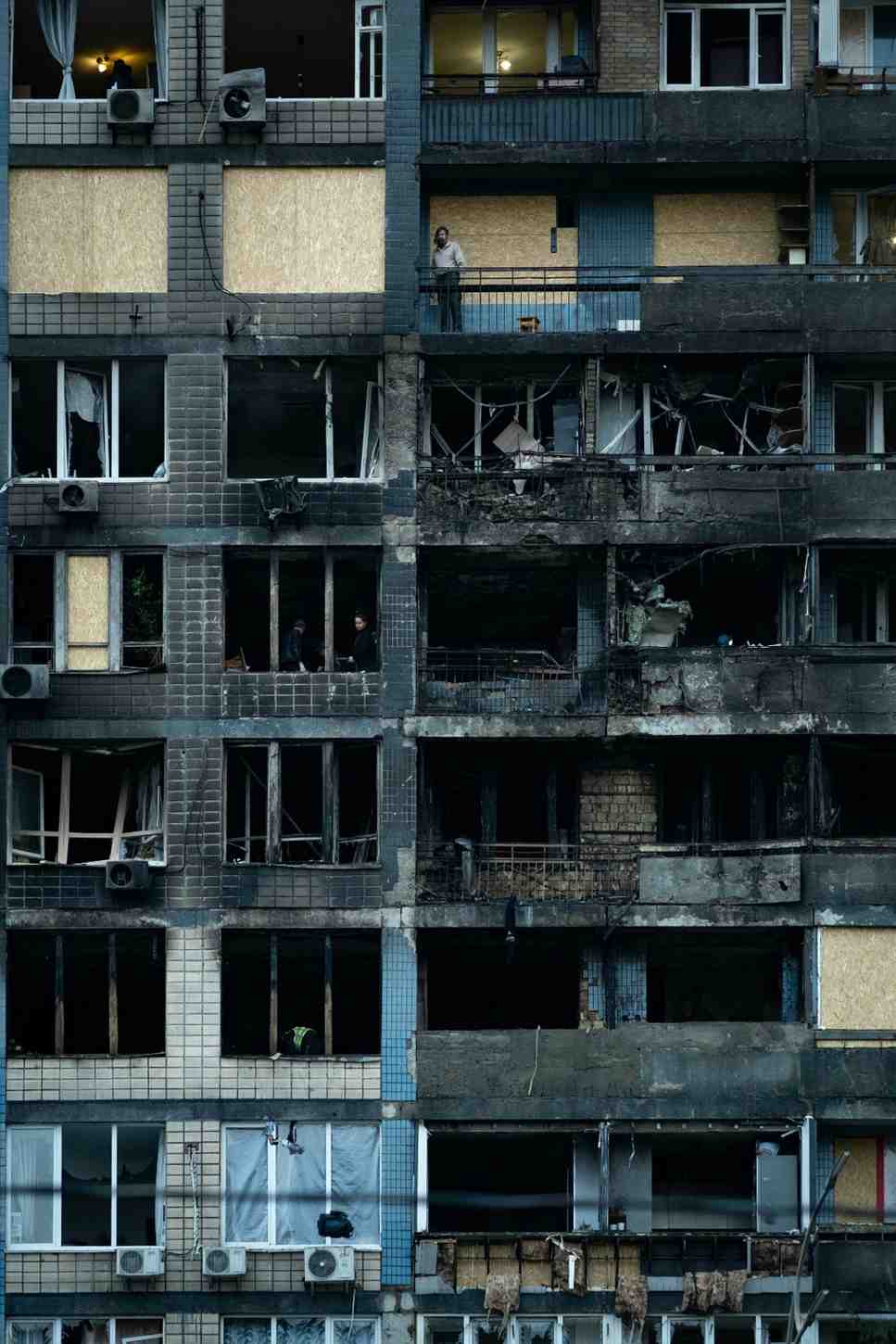 Severe fire damage on a multi-story apartment building exterior with charred walls and broken windows.