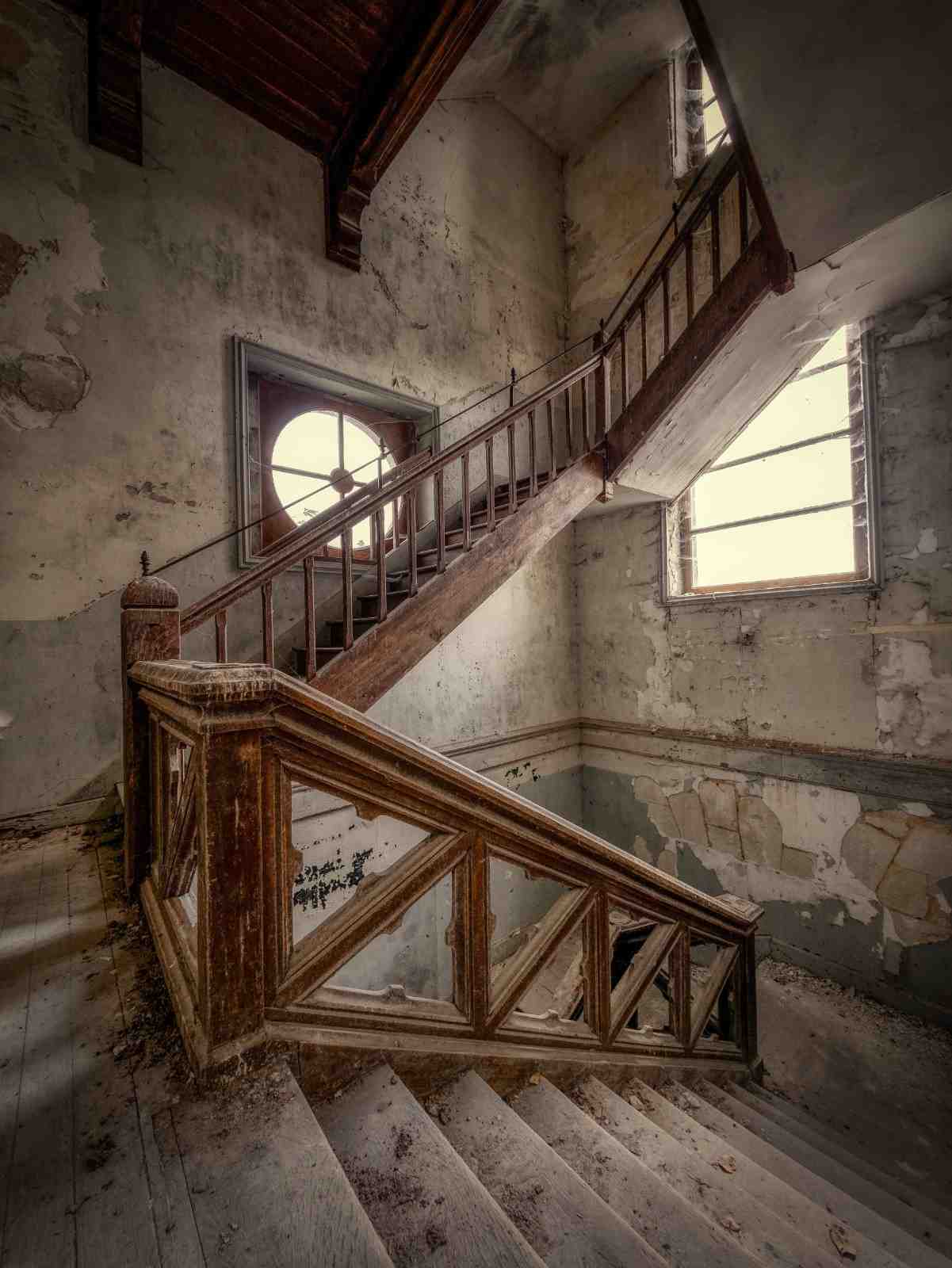 Dusty, dilapidated wooden staircase in an abandoned building with peeling paint and debris.