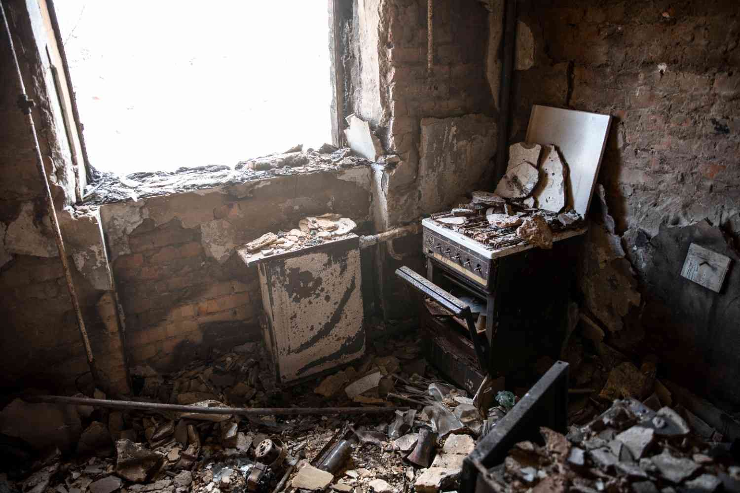 Severe structural fire damage in a ruined kitchen covered in brick debris.