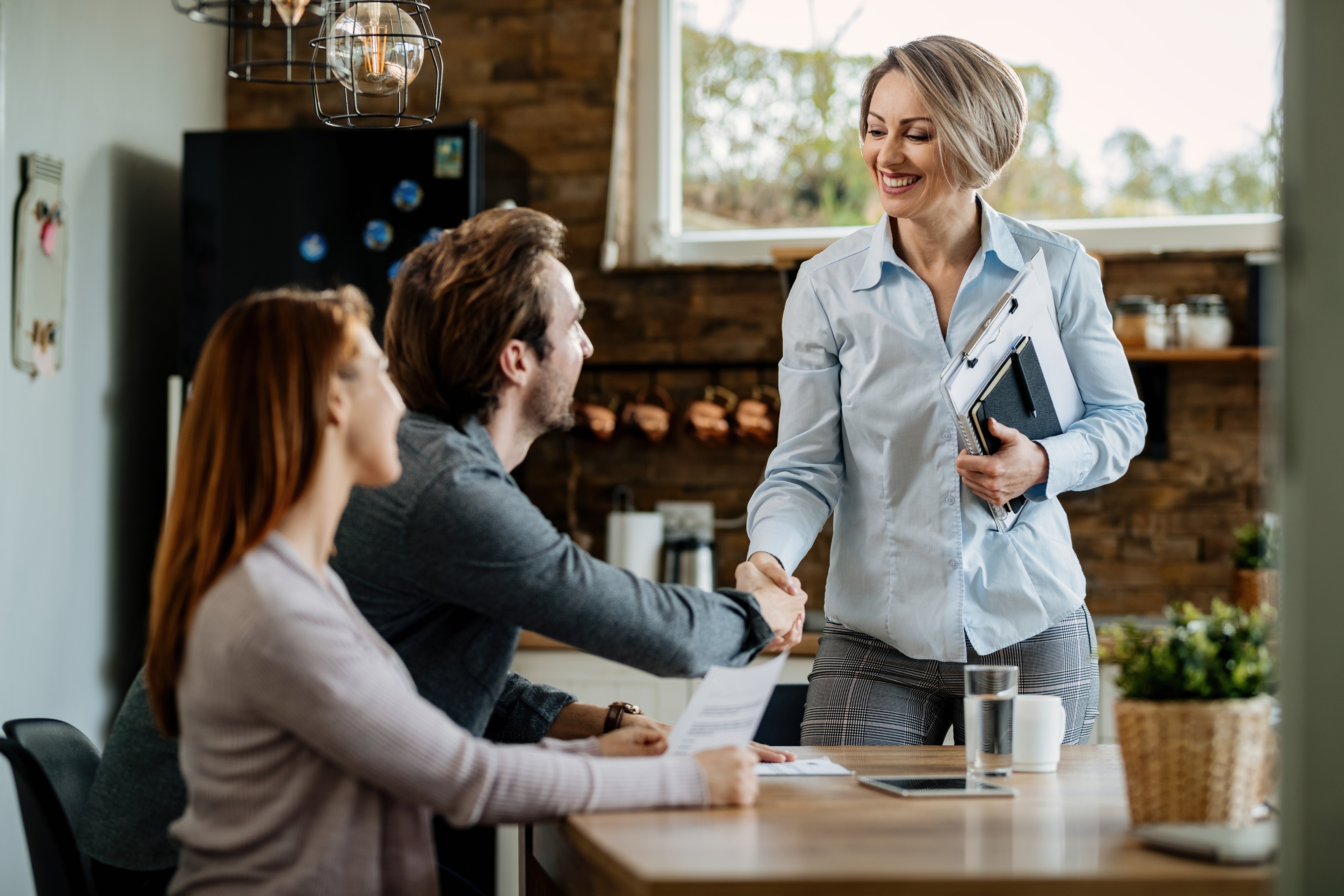A insurance specialist smiling and shaking hands with a relieved homeowner at their kitchen table after securing claim approval.