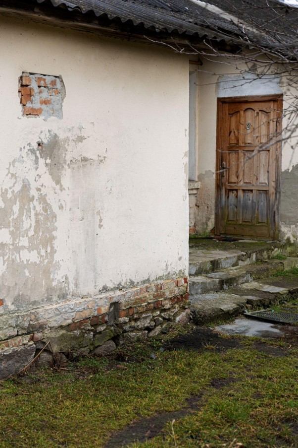 Peeling exterior wall paint and damp stone foundation indicating severe moisture and mold risks.