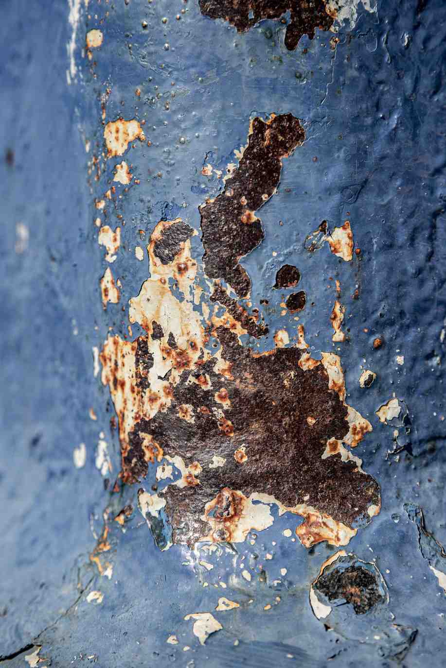 Severe moisture damage causing blue paint to peel, revealing heavy rust and decay on a metal surface.