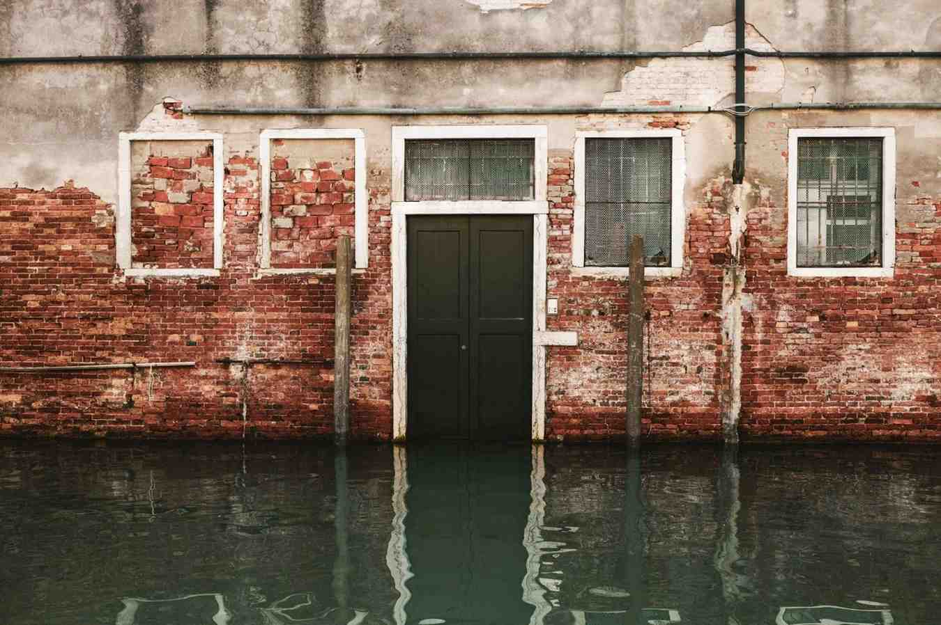 Flooding and structural water damage at the base of a brick building.
