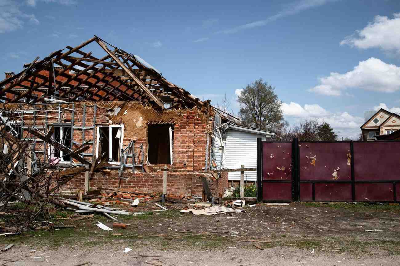 A severely damaged brick house with a destroyed roof and debris scattered in the yard.