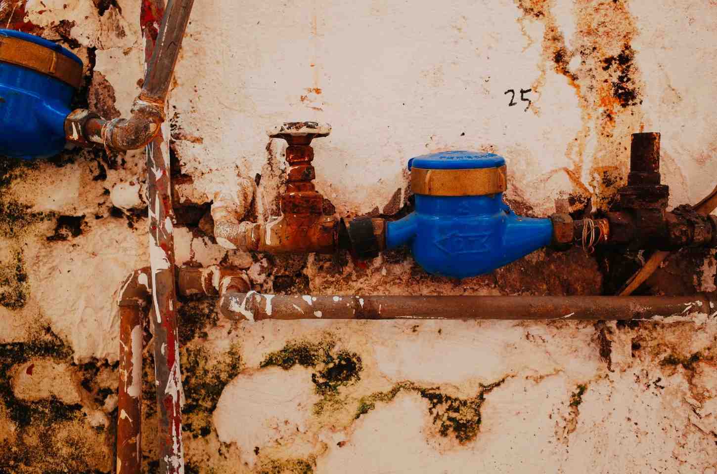 Corroded plumbing fixtures and moisture stains on a basement wall indicating a severe pipe leak.