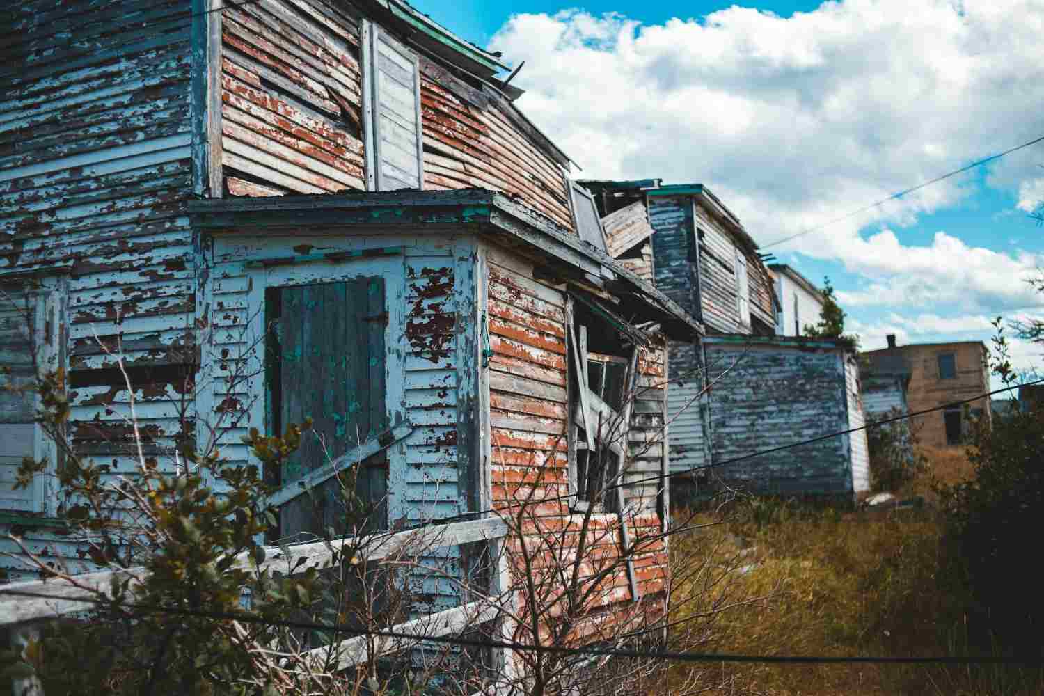 Dilapidated wooden home exterior with severe peeling paint indicating heavy water damage.