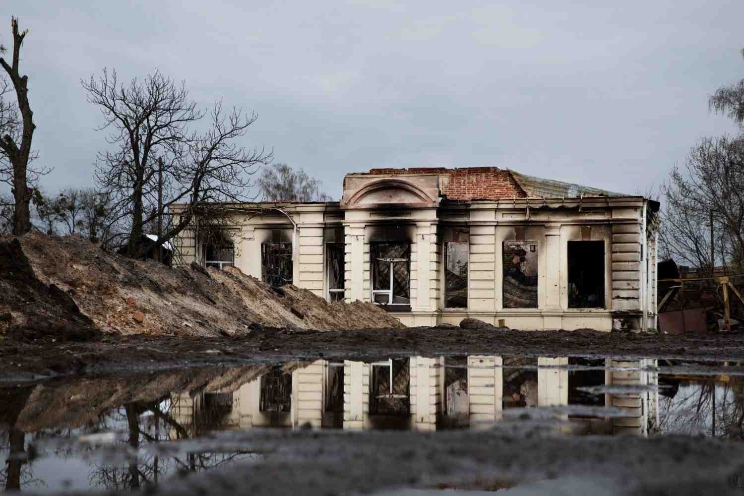 A large puddle of standing water reflecting a severely ruined building with extensive structural damage.