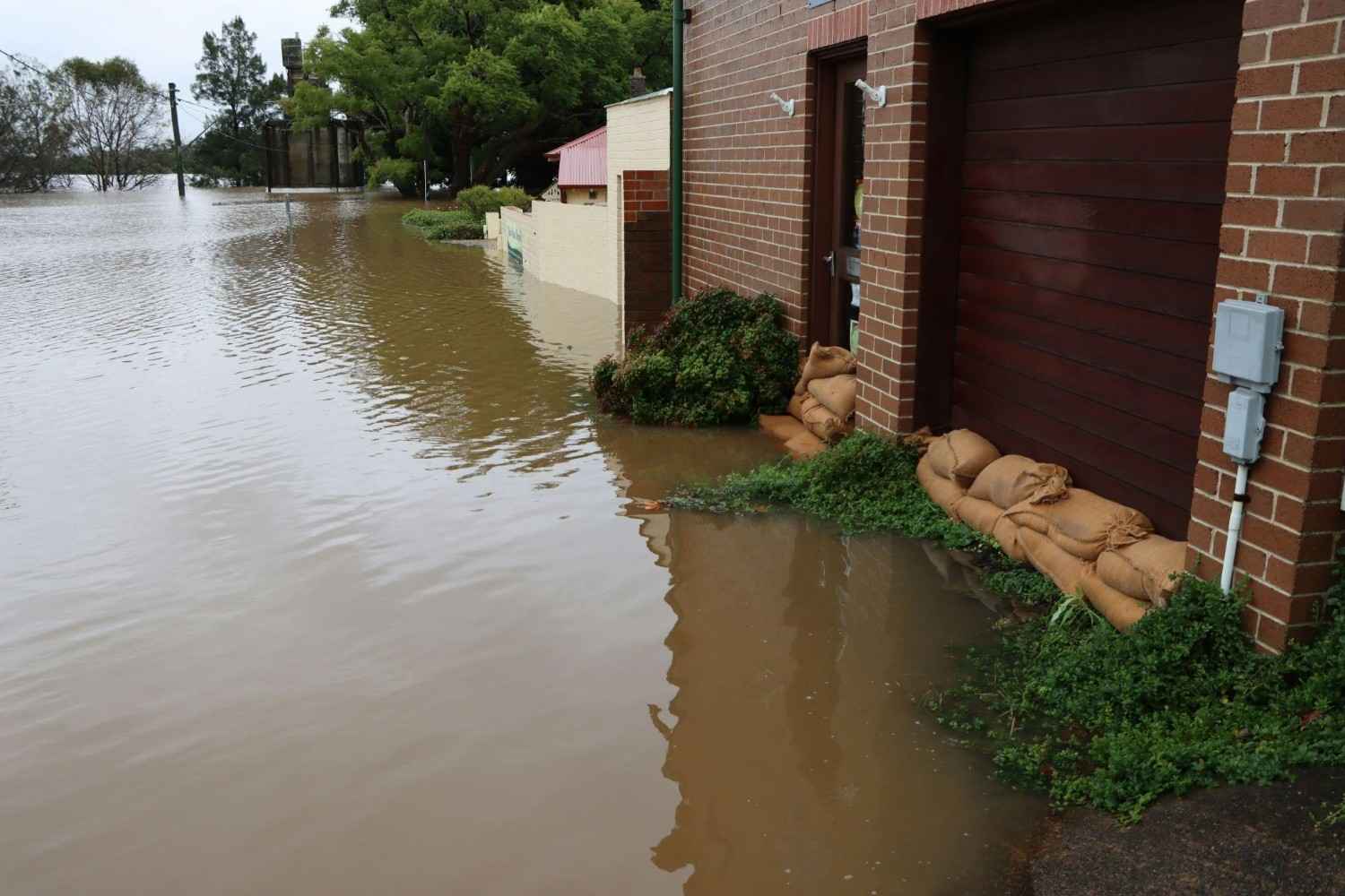 Brown floodwater surrounds a brick building protected by sandbags.