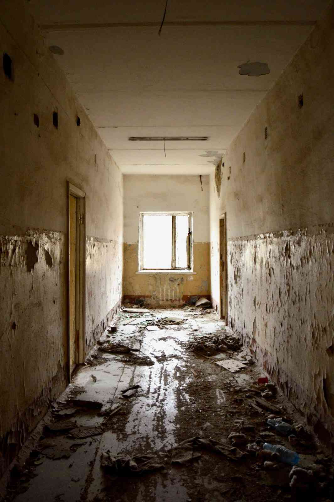 Severe indoor water damage in a dilapidated hallway, showing peeling paint, ruined walls, and floor debris.