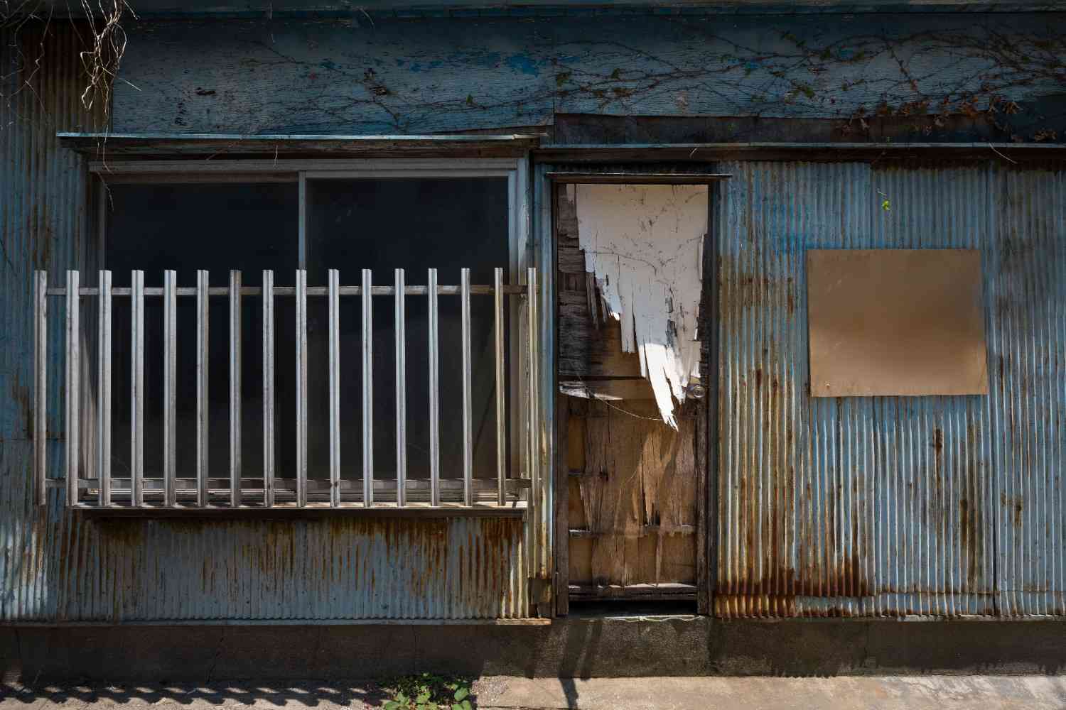 Rusted metal siding and a severely water-damaged peeling door on a deteriorating building exterior.