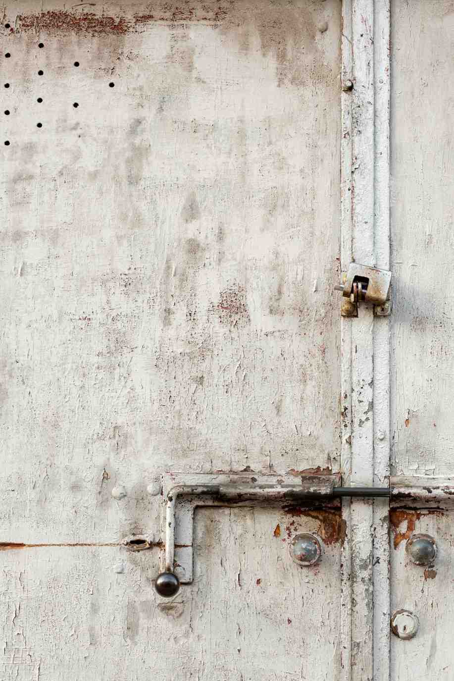Close-up of peeling white paint and rust on a metal door latch, indicating severe moisture and water damage.