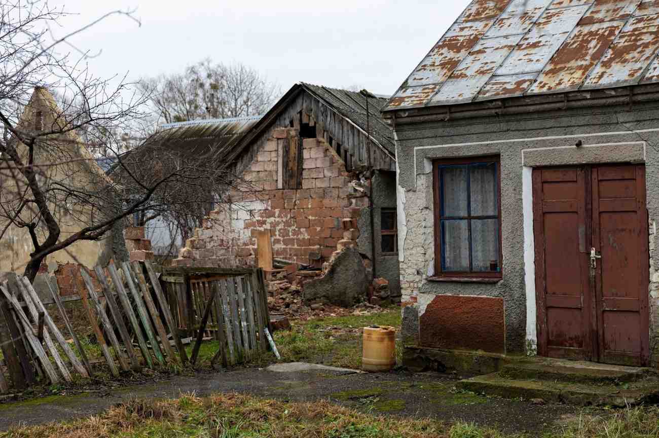 Decaying old house with exposed bricks and a boarded-up blue door.