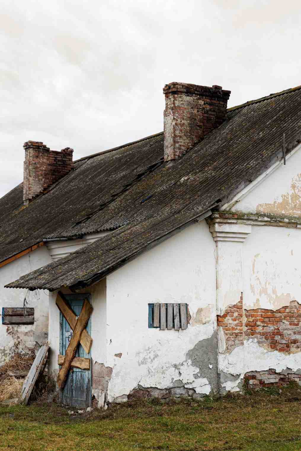 Dilapidated rural property with a crumbling brick wall and broken wooden fence.
