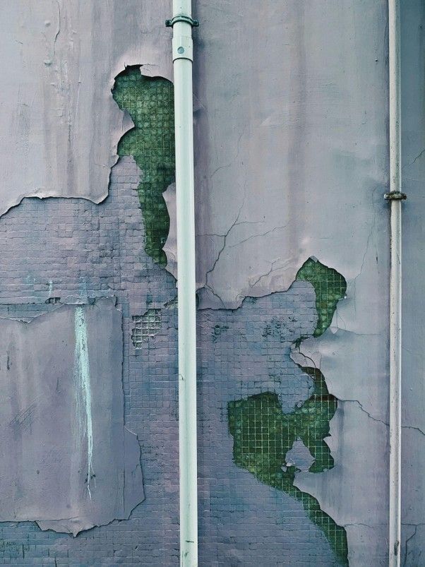 Severe structural water damage causing peeling wall paint and exposed tiles near a pipe.