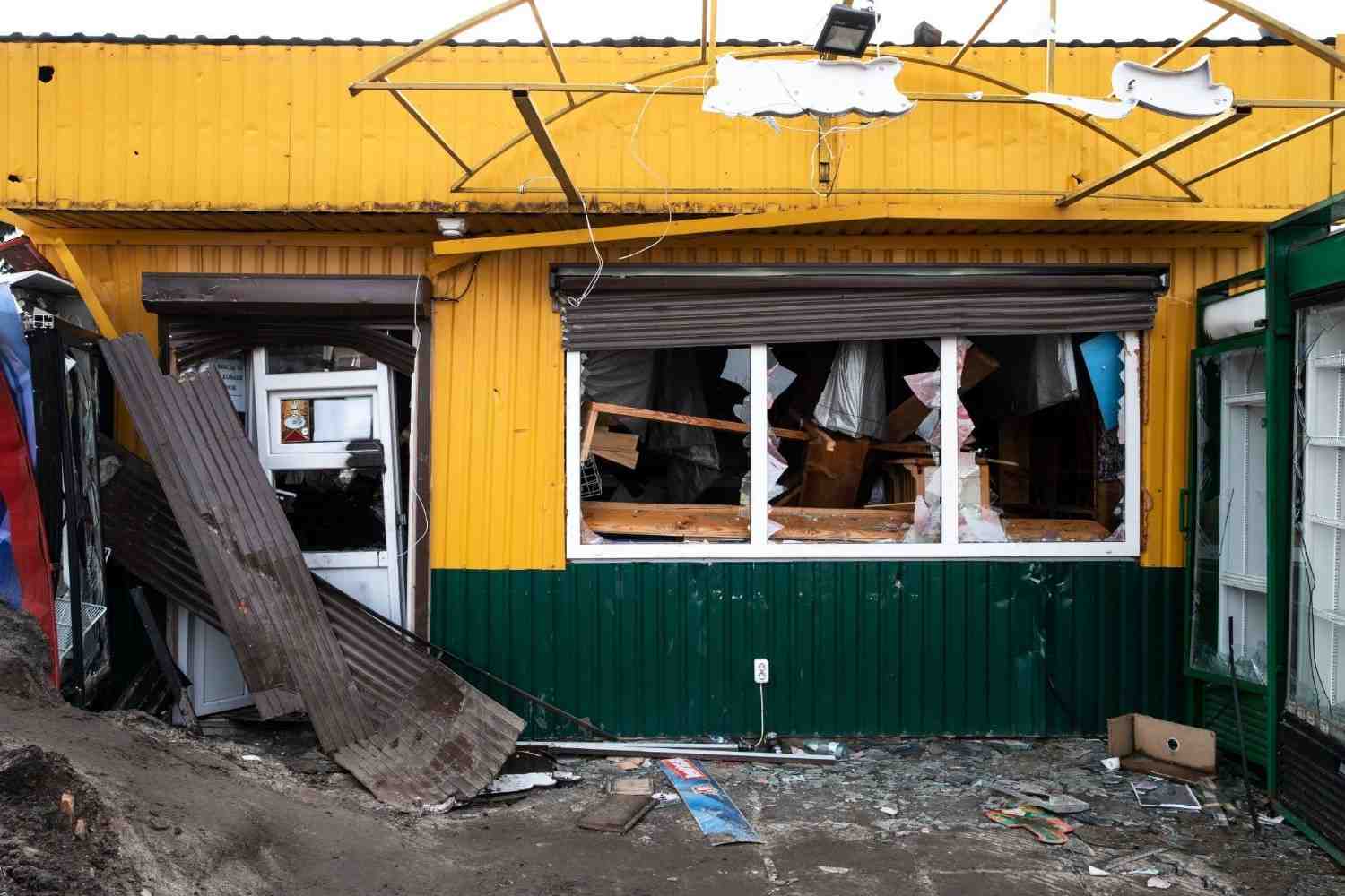 Severely damaged commercial storefront with shattered windows and torn metal roofing debris.